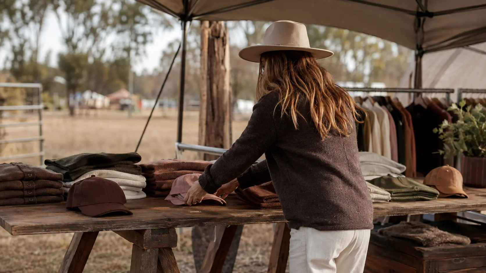 A stallholder in a wide-brimmed hat laying out folded clothing on a trestle table at a showground