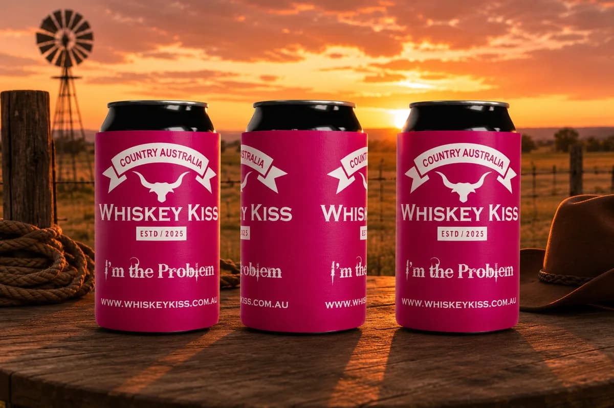 Three pink Whiskey Kiss stubby coolers on a timber table at sunset